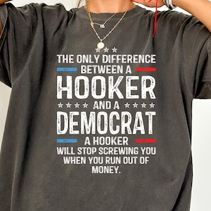 May include: Dark gray t-shirt with the text "THE ONLY DIFFERENCE BETWEEN A HOOKER AND A DEMOCRAT" in white. The shirt also includes the text "A HOOKER WILL STOP SCREWING YOU WHEN YOU RUN OUT OF MONEY."