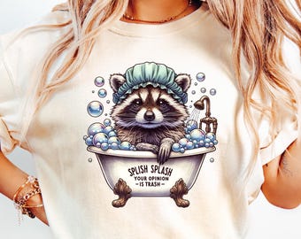 Könnte beinhalten: Cremefarbenes T-Shirt mit einem Waschbären in einer Badewanne mit Blasen und einem Duschkopf. Der Waschbär trägt eine blaue Duschhaube. Der Text auf der Wanne lautet "SPLISH SPLASH YOUR OPINION IS TRASH".