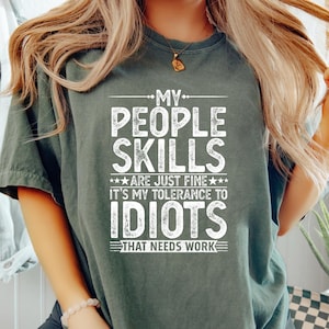 Könnte beinhalten: Dunkelgrünes T-Shirt mit dem weißen Text "MY PEOPLE SKILLS ARE JUST FINE IT'S MY TOLERANCE TO IDIOTS THAT NEEDS WORK". Das Shirt hat einen lässigen Stil, mit Rundhalsausschnitt und kurzen Ärmeln. Der Text ist fett und ohne Serifen.