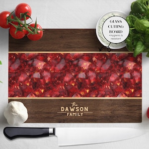 Può includere: Un tagliere rettangolare in legno con un centro a fantasia rosso e oro e un bordo marrone scuro. Il testo "The DAWSON FAMILY" è stampato in basso. Sono presenti anche una ciotola bianca, pomodori e un coltello.