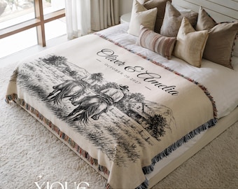 May include: A cream-colored woven throw blanket featuring a black ink-style illustration of two people riding horses through a field. The text reads Oliver & Amelia and October 20 2027. The blanket has a fringed edge with multi-colored threads.