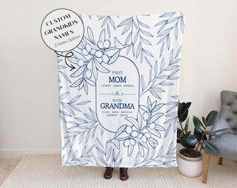 May include: White blanket with a blue floral design and text. The text reads "First Mom, Now Grandma" with names below. The blanket has a custom grandkids names option and comes in 3 sizes.
