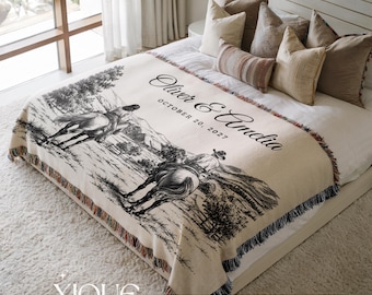 May include: A cream-colored woven throw blanket featuring a black ink-style illustration of two people riding horses through a landscape. The text reads Oliver & Amelia October 20, 2027. The blanket has a fringed edge with multi-colored threads.