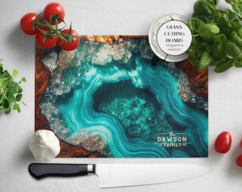 May include: A rectangular glass cutting board with a teal and brown agate design. The board has the text "The Dawson Family" in gold. A white chef's knife, tomatoes, and herbs are arranged around the board.