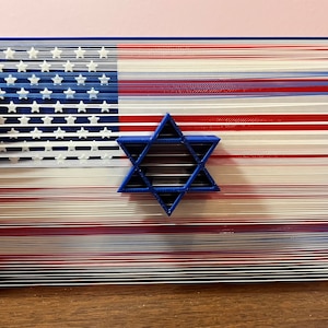 Op de afbeelding: Een blauwe en witte Amerikaanse vlag wordt getoond in een 3D-string art-ontwerp. Een blauwe Davidster is gecentreerd op de vlag.