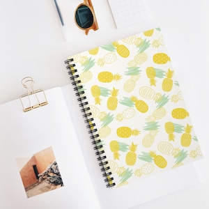 May include: A white spiral notebook with a yellow and green pineapple pattern. The notebook has a white background with yellow pineapples and green leaves.