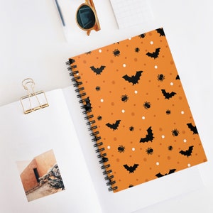 May include: Orange spiral notebook with a black bat and spider pattern. The notebook has white polka dots.