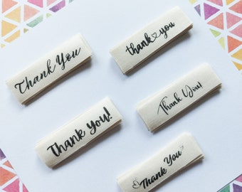 May include: Five white fabric labels with black text. The labels say "Thank You" in different variations, including "Thank You!" and "thank you".