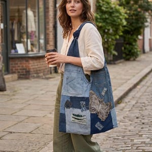 May include: A denim patchwork tote bag with a butterfly design. The bag is made from various shades of blue denim, with pockets and distressed details. The butterfly is light brown. The bag is carried over the shoulder.