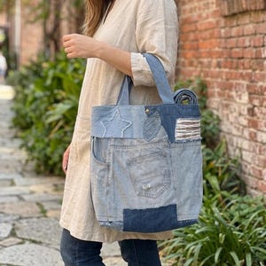 Puede incluir: Bolso tote de mezclilla con diseño patchwork. El bolso presenta detalles de estrella, hoja y rayas. Tiene un bolsillo frontal grande y asas resistentes. El bolso está hecho de mezclilla reciclada y tiene una estética casual y rústica.