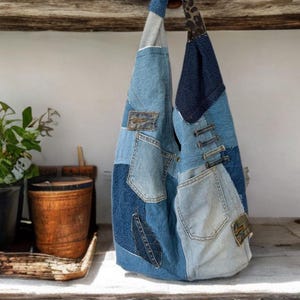 May include: A patchwork denim tote bag in various shades of blue. The bag has multiple denim pockets and a leaf-shaped patch. The handle combines denim and leopard print fabric. The bag is suspended from a wooden hook.