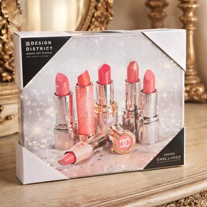 Puede incluir: Impresi&oacute;n en lienzo enmarcada con seis barras de labios en varios tonos de rosa y coral. Las barras de labios est&aacute;n en tubos plateados y dorados, con una tumbada de lado. El fondo es un dise&ntilde;o brillante y claro. El texto "DESIGN DISTRICT" es visible.