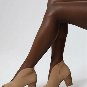 May include: Tan suede peep-toe booties with a high block heel. The ankle boots have a V-shaped cut on the sides. The shoes are a neutral color and have a classic design.