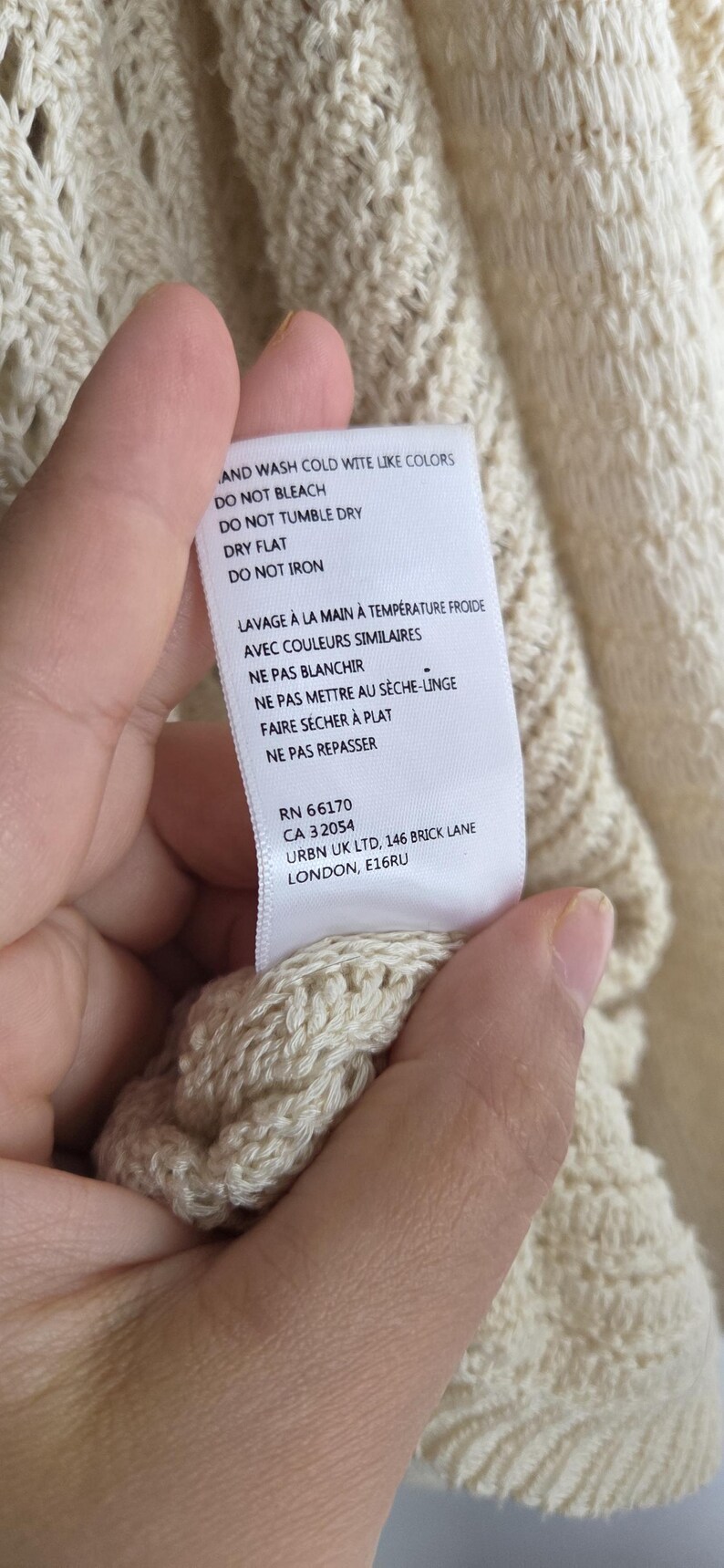 May include: Cream-colored knitwear with a textured pattern. A tag with care instructions is visible. The tag includes washing instructions, such as "wash cold with like colors" and "do not bleach."