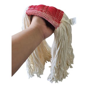 May include: A white cotton mop head with a red mesh top is held in a hand. The mop head has long, thick strands of absorbent cotton. A tag is attached to the top of the mop head.