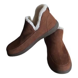 May include: A pair of brown suede ankle boots with a soft, white faux fur lining. The boots have a low profile and a dark brown sole. The design is simple and comfortable, suitable for casual wear.