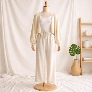 May include: A cream-colored outfit on a mannequin. The outfit includes a cropped cardigan with balloon sleeves, a white tank top, and wide-leg pants. The outfit is displayed on a wooden mannequin stand.