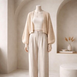 May include: A cream-colored outfit on a mannequin. The outfit includes a cropped, open-front cardigan with balloon sleeves, a tank top, and high-waisted, wide-leg pants. The ensemble is a neutral color, creating a cohesive and minimalist aesthetic.