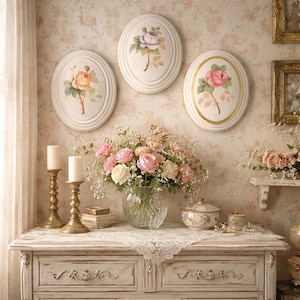May include: A vintage-style room with floral wallpaper and a white dresser. Three oval wall plaques with rose paintings hang above the dresser. A bouquet of pink and white roses sits in a glass vase on the dresser, along with candles and decorative items.