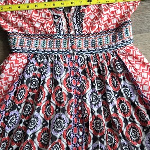 May include: A vibrant sundress with a V-neck and floral patterns in red, black, and purple. The dress has a button-down front and a fitted waist. The dress measures approximately 33 cm across the chest.