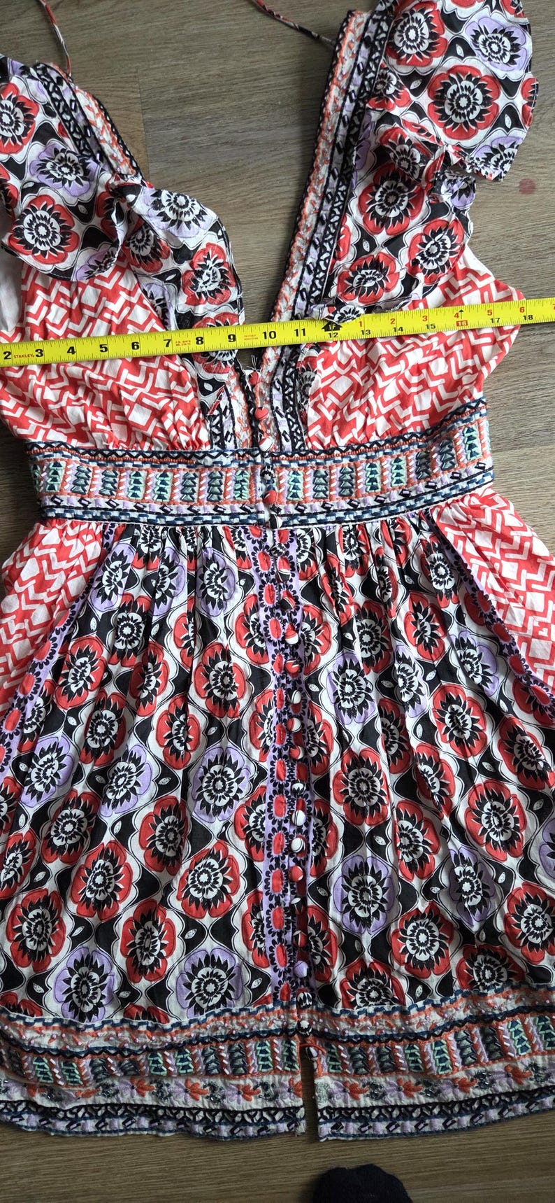 May include: A vibrant sundress with a V-neck and floral patterns in red, black, and purple. The dress has a button-down front and a fitted waist. The dress measures approximately 33 cm across the chest.