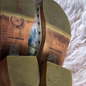 May include: Pair of wooden-soled clogs with floral fabric uppers and studded accents. The soles are marked "Made in India" and size 38. The clogs have a light brown wooden base and a rubber sole.