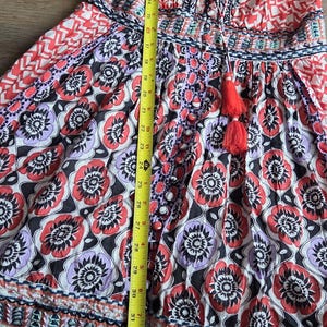 May include: A patterned dress with a V-neck and tassel detail. The dress features a floral print in red, black, and purple, and measures approximately 89 cm in length. It is hanging on a white hanger.