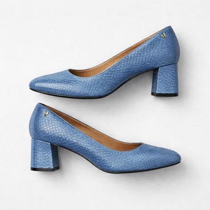 May include: Two pairs of light blue, textured leather pumps with block heels. Each shoe has a small gold emblem near the heel. The shoes have a classic, rounded toe design and a neutral-colored interior.