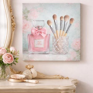 Puede incluir: Una botella de perfume rosa con un lazo y un juego de brochas de maquillaje en un soporte de vidrio. El fondo presenta un dise&ntilde;o floral con rosas. La botella de perfume tiene la marca "Chanel".