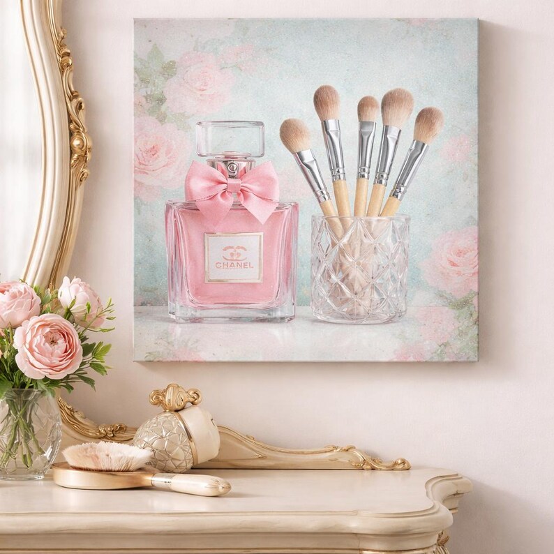 Puede incluir: Una botella de perfume rosa con un lazo y un juego de brochas de maquillaje en un soporte de vidrio. El fondo presenta un dise&ntilde;o floral con rosas. La botella de perfume tiene la marca "Chanel".