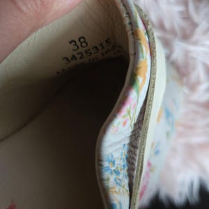 May include: Close-up of the inside of a beige shoe, size 38, with a floral patterned lining. The shoe's interior is visible, showing the stitching and materials. The floral pattern includes blue, pink, and yellow flowers.