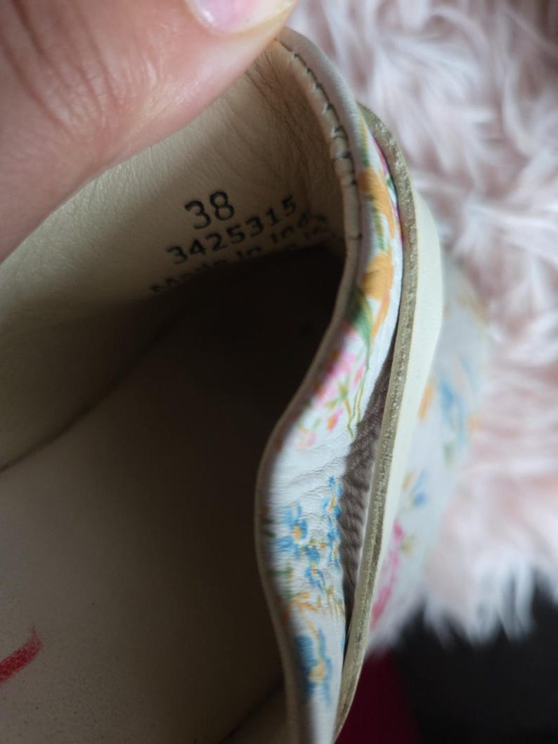 May include: Close-up of the inside of a beige shoe, size 38, with a floral patterned lining. The shoe's interior is visible, showing the stitching and materials. The floral pattern includes blue, pink, and yellow flowers.