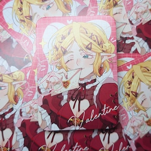 May include: A stack of Valentine's Day themed cards featuring an anime-style illustration of a blonde character with elf ears. The character is wearing a red dress and holding a heart-shaped object. The word "Valentine" is written on the cards.