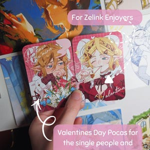 May include: Two Valentine's Day cards featuring anime-style illustrations of characters with blonde and brown hair, red and white outfits, and the text "Please Be Mine" and "Valentine". The cards are held in a hand, with the text "Valentines Day Pocas for the single people and the couples".
