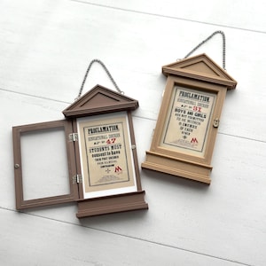 Puede incluir: Dos letreros de proclamación enmarcados en madera con colgadores de cadena. Uno está abierto, revelando un aviso impreso con texto. El otro está cerrado. El texto en los letreros dice "PROCLAMATION" y "EDUCATIONAL DECREE".