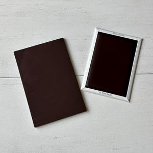 K&ouml;nnte beinhalten: Zwei rechteckige schwarze magnetische Oberfl&auml;chen. Eine ist eine einfache schwarze Oberfl&auml;che. Die andere ist wei&szlig; umrahmt mit dem aufgedruckten Text "BE FUN SHOP" und "52 MAGNETS".