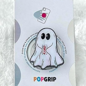 May include: A PopSockets PopGrip phone accessory in original packaging. The grip features a white ghost illustration holding a red and white Coca-Cola can. The packaging includes the brand name PopSockets, the text PopGrip, and instructions.