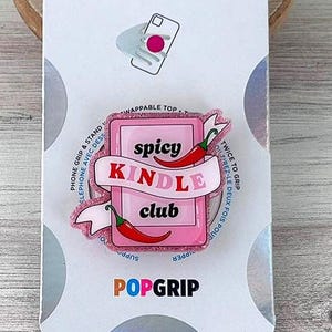 May include: A pink PopSocket phone grip with the words "spicy Kindle club" and two red chili pepper illustrations. The PopSocket is attached to a white card with the PopSockets logo and a diagram of a phone.