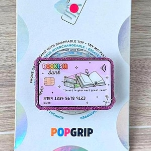 May include: A PopSockets PopGrip featuring a pink and purple design with the words "BOOKISH bank" and a graphic of books. The PopGrip has a credit card design with the numbers 3759 1234 5678 9123.