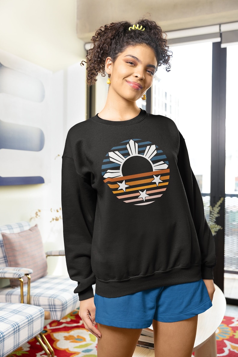 May include: A black sweatshirt with a retro-style graphic of the Philippine flag. The graphic features a sun with rays, three stars, and stripes in shades of blue, orange, and pink.