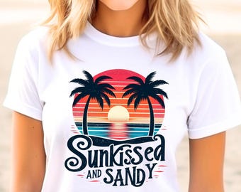 Può includere: Maglietta bianca con una grafica di due palme e un tramonto con il testo "Sunkissed and Sandy".