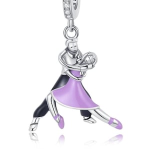 以下が含まれることがあります： タンゴを踊るカップルを描いたシルバーチャーム。女性は紫色のドレス、男性は黒いスーツを着ています。チャームはクリアなキュービックジルコニアで飾られています。