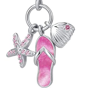 Puede incluir: Un charm de plata con temática playera. Presenta una estrella de mar, una chancla y una concha, todos en rosa y plata. El charm tiene un lazo para sujetarlo a una pulsera o collar. Una pequeña gema transparente está engastada en el lazo superior.