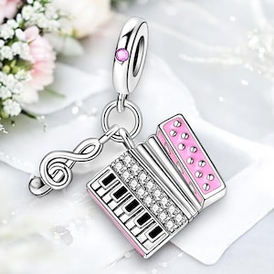 Puede incluir: Un charm de plata con forma de acordeón con un diseño rosa y blanco. El charm tiene una clave de sol unida a él y está decorado con cristales transparentes.