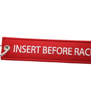 Può includere: Portachiavi in ​​tessuto rosso con un anello portachiavi argentato. Il portachiavi è ricamato in bianco con la scritta "INSERT BEFORE RACE".
