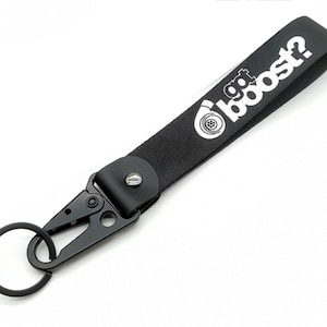 Puede incluir: Llavero de cuero negro con un anillo de llave de metal y un logotipo en blanco y negro que dice "got boost?" con un símbolo de turbocompresor.
