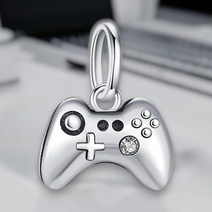 Peut inclure: Charme argenté en forme de manette de jeu vidéo avec un cristal transparent au centre.