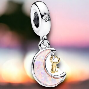 May include: A silver charm featuring a white opal crescent moon with a gold key hanging from it. The charm has a silver star with a clear crystal on top.