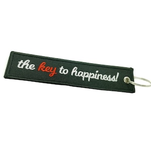May include: Black fabric keychain with white text that reads "the key to happiness!" in a cursive font. The word "key" is in red.