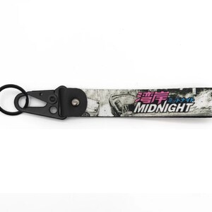 Peut inclure: Porte-clés noir et blanc avec une voiture et le texte "MIDNIGHT" en rose et bleu. Le texte en japonais dit "Midnight".